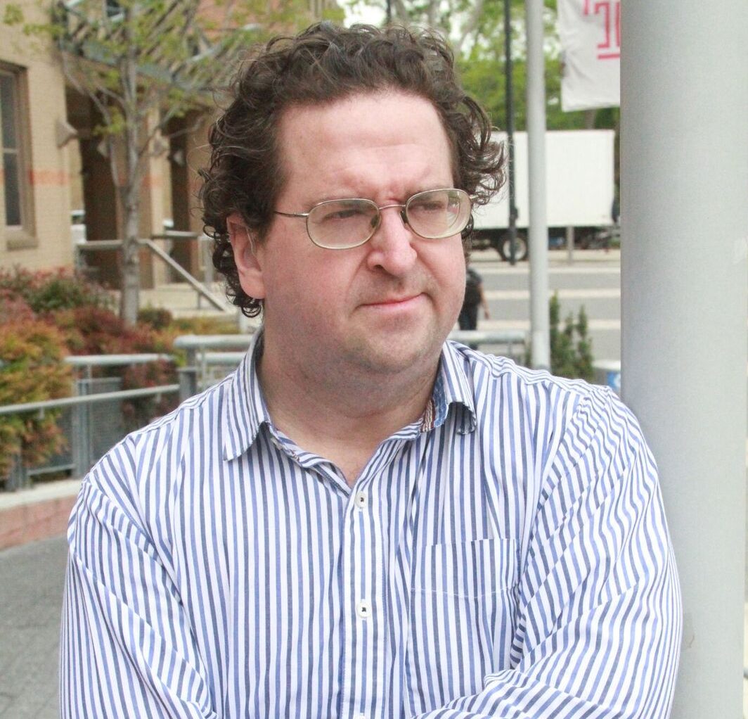 Man in glasses and workshirt with his arms crossed as if thinking.